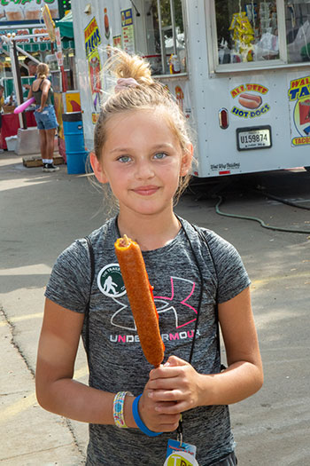 Girl eating a footlong corndog.